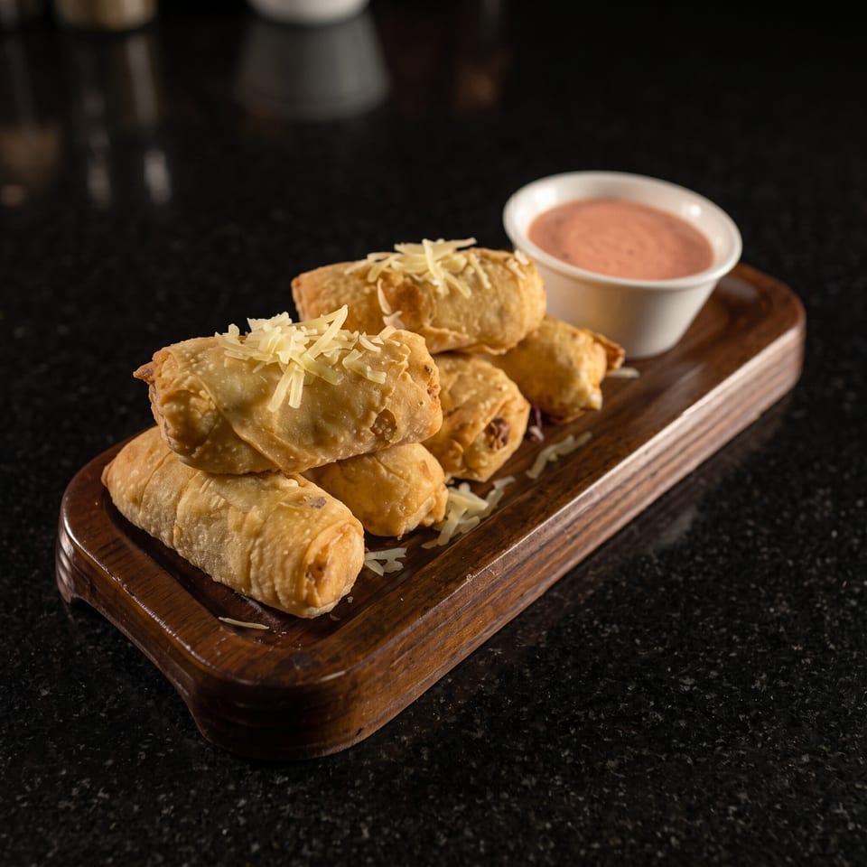 Golden fried stuffed pastries topped with shredded cheese, served on a wooden platter with dipping sauce.